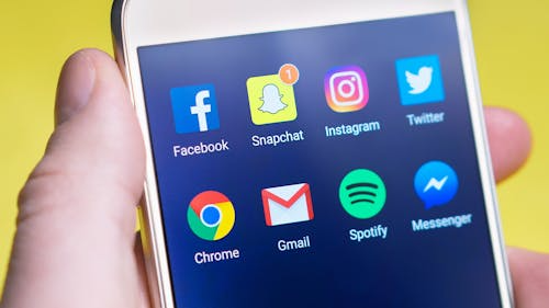 Hand holding a smartphone displaying various social media applications